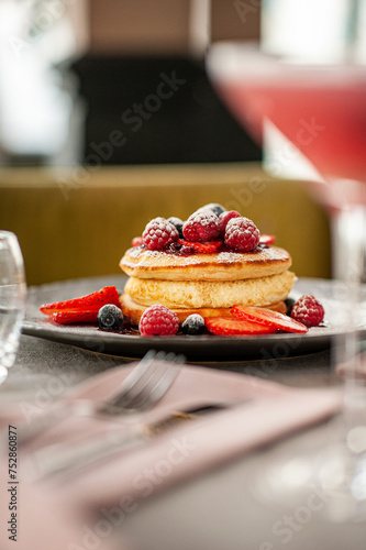 Homemade fluffy pancake with fruits and cream on the top  on a coffee shop table. Side view