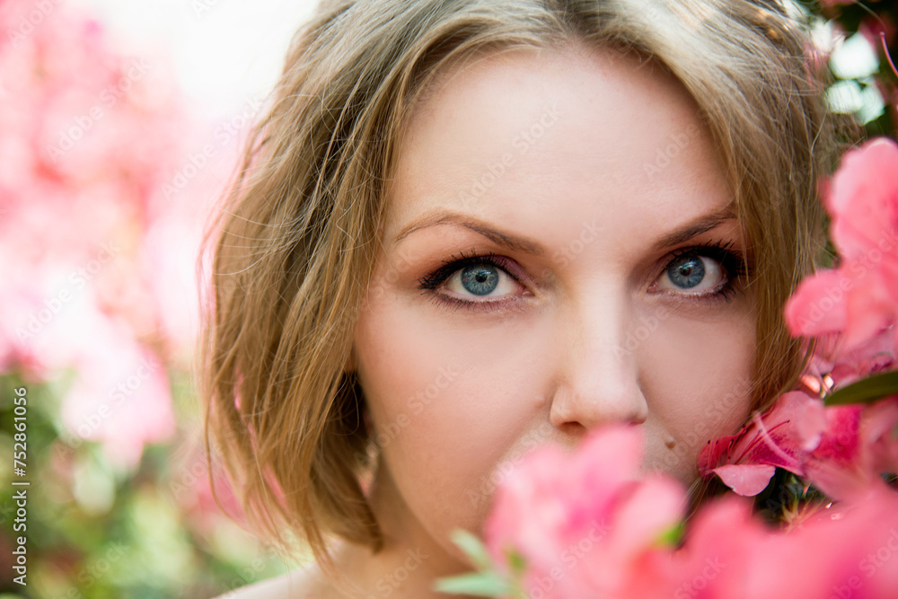 closeup portrait of beautiful blonde sexy smiling romantic girl in a pink dress waking in botanical garden with blossoming flowers azaleas on sunny day