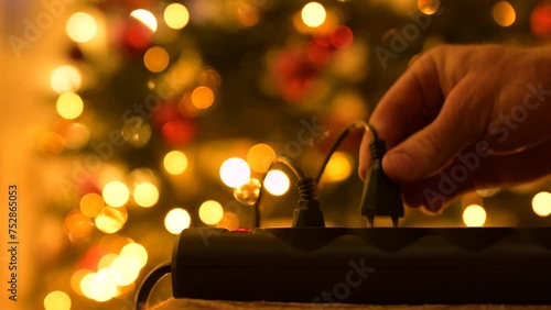 Close up on hand plugging Christmas lights garlands to outlet. Turning on Christmas tree, lights on, festive mood