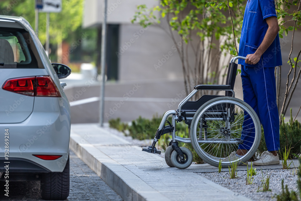 Male nurse with a wheelchair waiting for a patient near the car