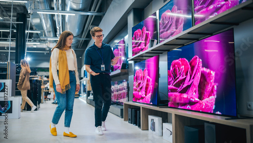 Young Female Shopper Having Conversation with Electronics Store Sales Rep. Stylish Lady Explores Sleek Flat-Screen TV Options. Customer Seeking Impressive Television Solutions in Retail Store. photo