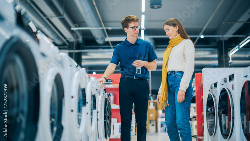 Customer Engages in Dialogue with a Retail Electronics Shop Consultant while Choosing a Washing Machine. Female Searching for a Laundry Appliance. Shopper Exploring Products in Modern Retail Store