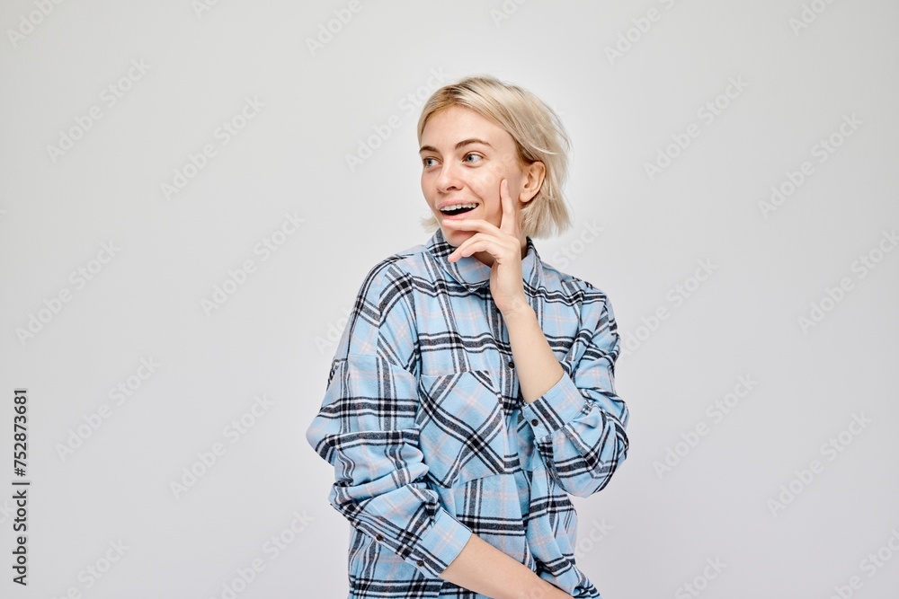 Young woman in plaid shirt looking uncertain, hand on chin, against a grey background. Young woman in plaid shirt looking uncertain, hand on chin, against a grey background.