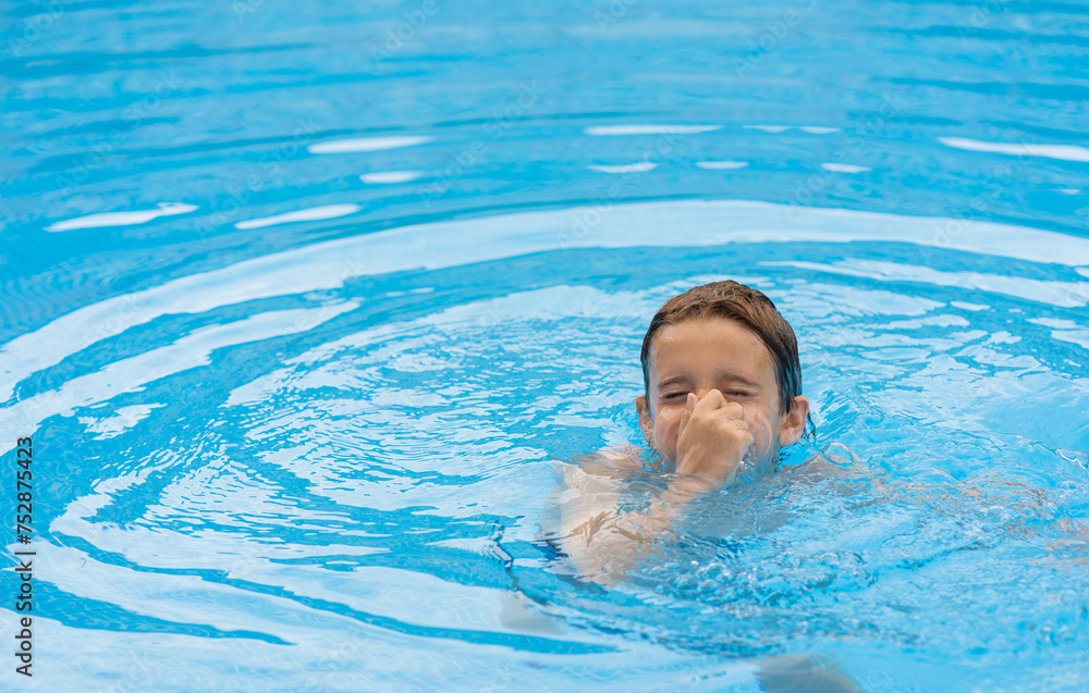 adorable boy diving into the blue pool, while holding his nose