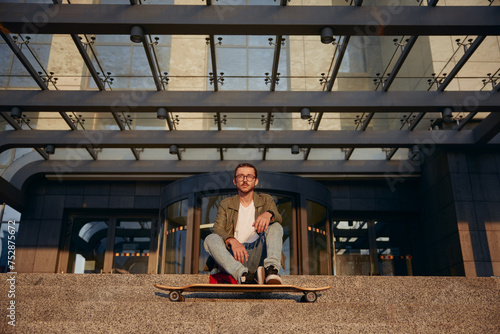 Cool guy student with longboard rest on stairs of university urban building
