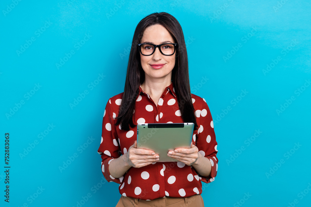 Portrait of cheerful pleasant girl wear red shirt in eyewear holding tablet in hands on interview isolated on blue color background Portrait of cheerful pleasant girl wear red shirt in eyewear holding tablet in hands on interview isolated on blue color background