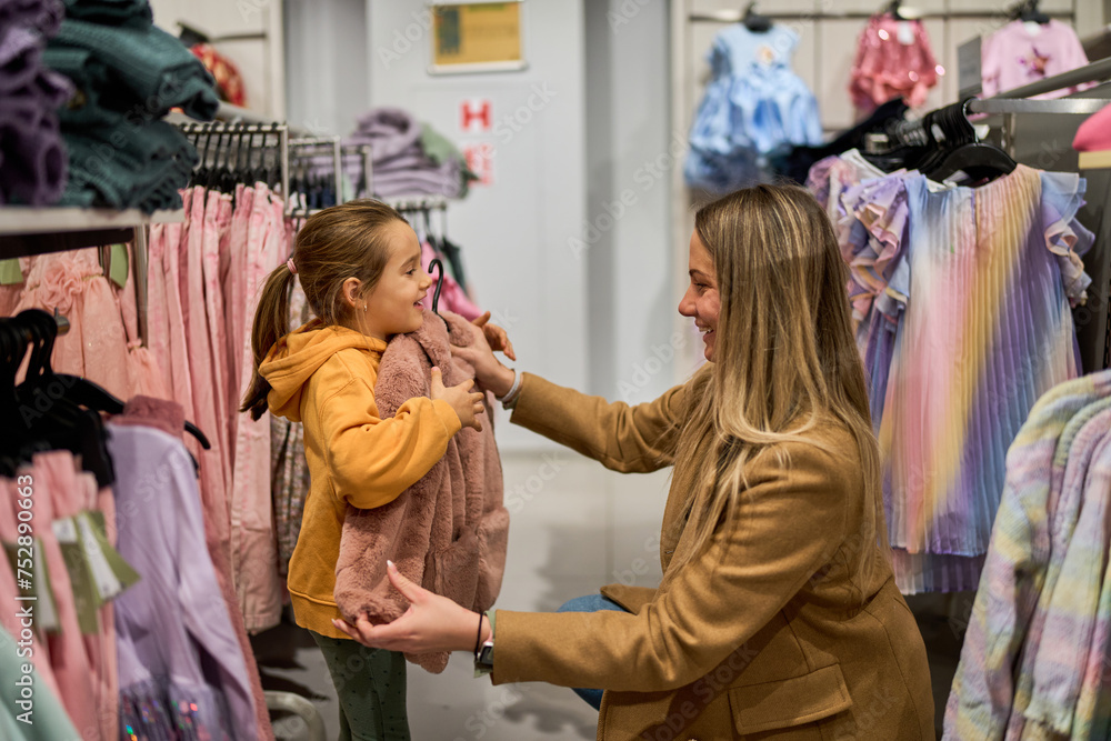 The mom shows her daughter a piece of clothing she wants to buy, pressing it against her to check the size and envisioning how it will look.