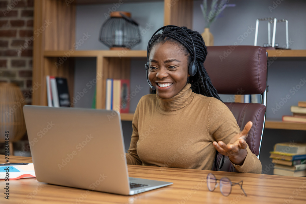 Adult woman with dreadlocks in headphones conducts virtual training using laptop Adult woman with dreadlocks in headphones conducts virtual training using laptop