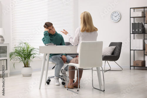 Psychologist working with teenage boy at table in office