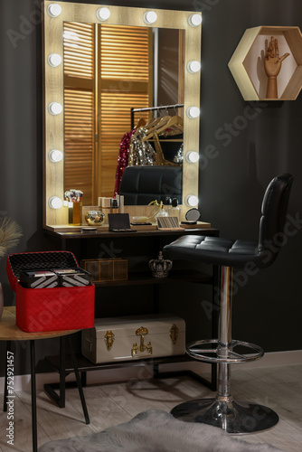 Makeup room. Stylish mirror near dressing table with beauty products and chair indoors