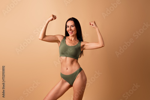No retouched photo of positive healthy woman standing with raised arms showing biceps isolated on beige color background © deagreez