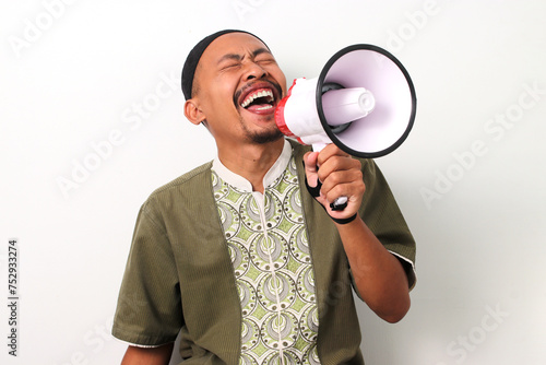 Excited Indonesian Muslim man in koko and peci shouts into a megaphone, announcing Ramadan sales and special offers. Isolated on a White background