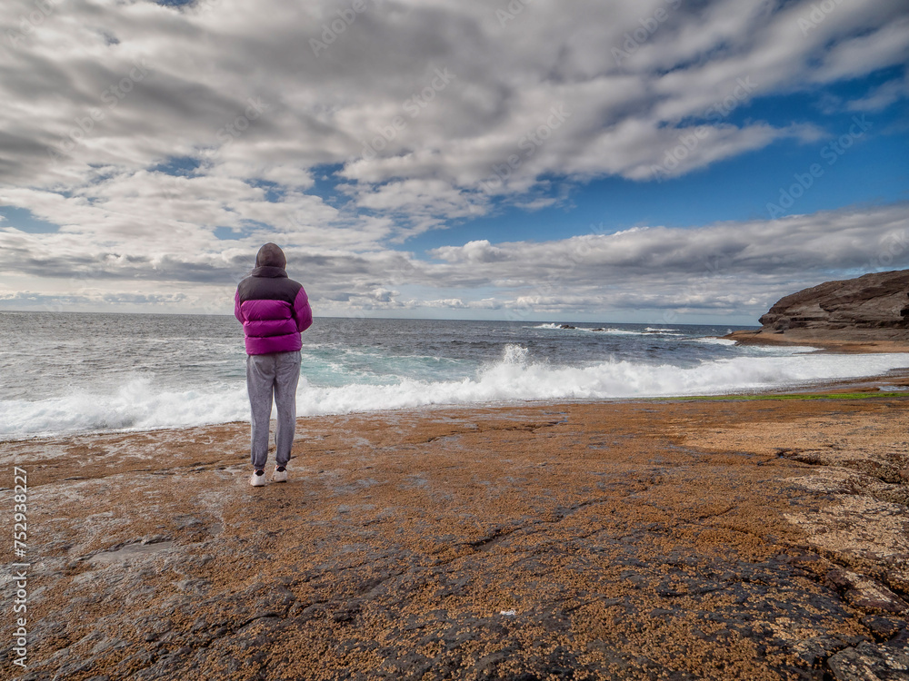 Teenager girl looking at stunning nature scenery with ocean and rough stone shore and cloudy sky. Kilkee area, Ireland. Travel and sightseeing landmark Irish landscape. Warm sunny day