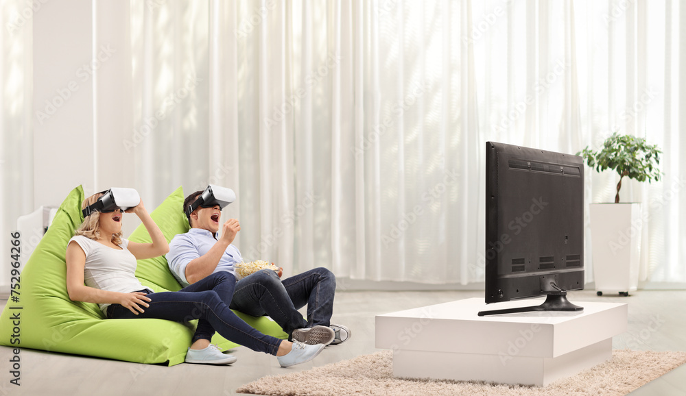 Excited young couple watching with virtual reality headsets seated on beanbags