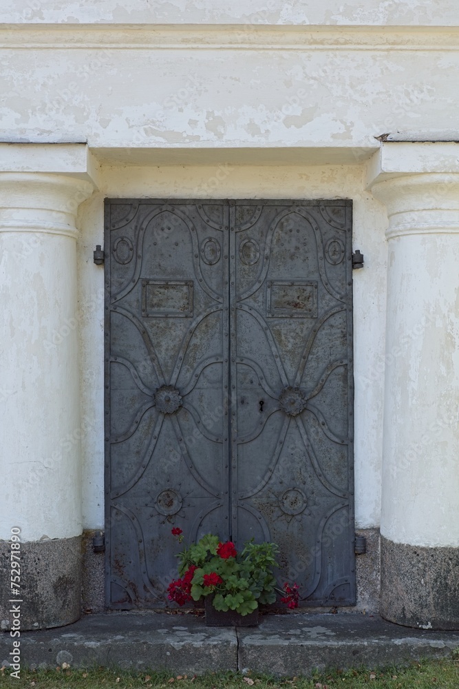 Fototapeta premium A decorative metal double doors with flowers in a vase at a old stone building.