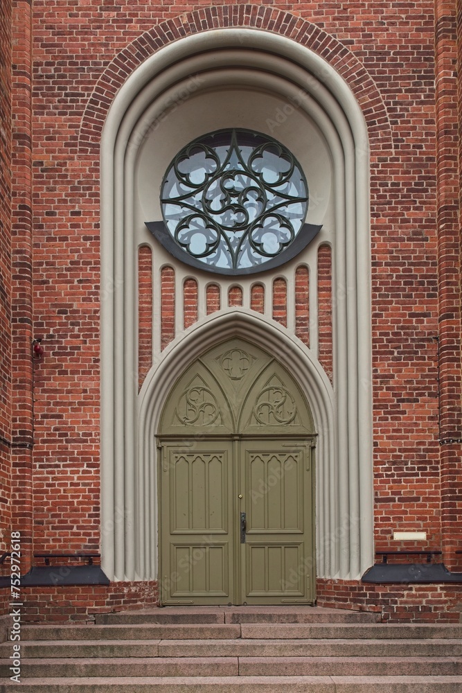 A wooden door with arch and round window on a red brick old building.