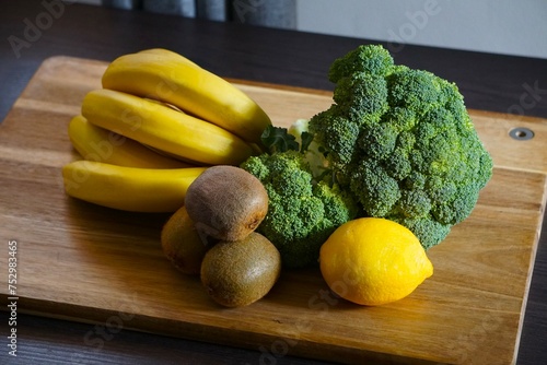 Banany, brokuł, kiwi i cytryna. Świeże owoce i warzywa leżą na desce do krojenia. Produkty przeznaczone do zdrowej diety.