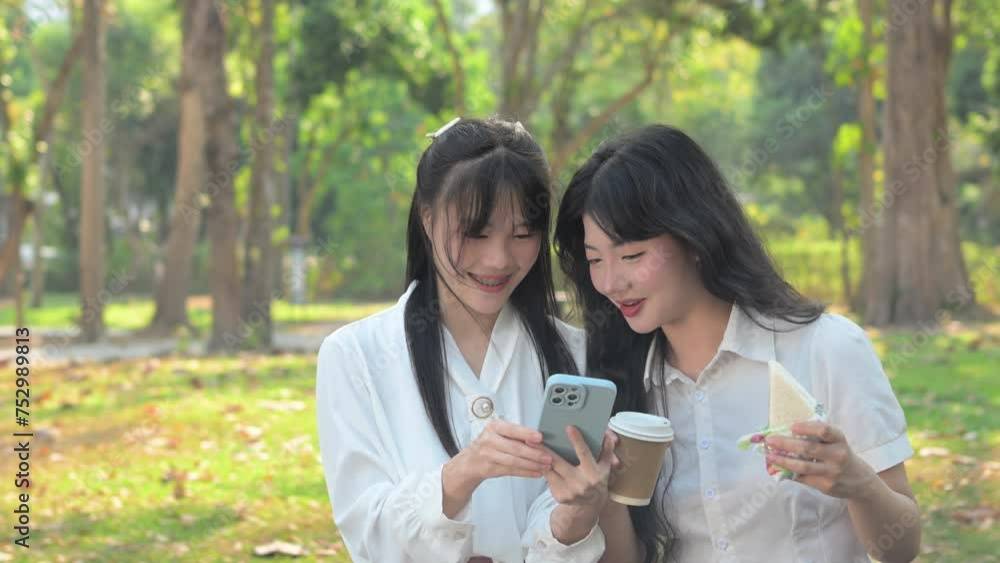 Shot of happy Asian female colleagues enjoying sandwich during lunch break and using mobile phone Shot of happy Asian female colleagues enjoying sandwich during lunch break and using mobile phone