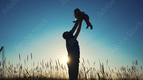 Fototapeta Naklejka Na Ścianę i Meble -  father throws play baby in the park. father's day silhouette happy family child dream concept. father plays with baby throws up. dad play his son in nature in the lifestyle park silhouette at sunset