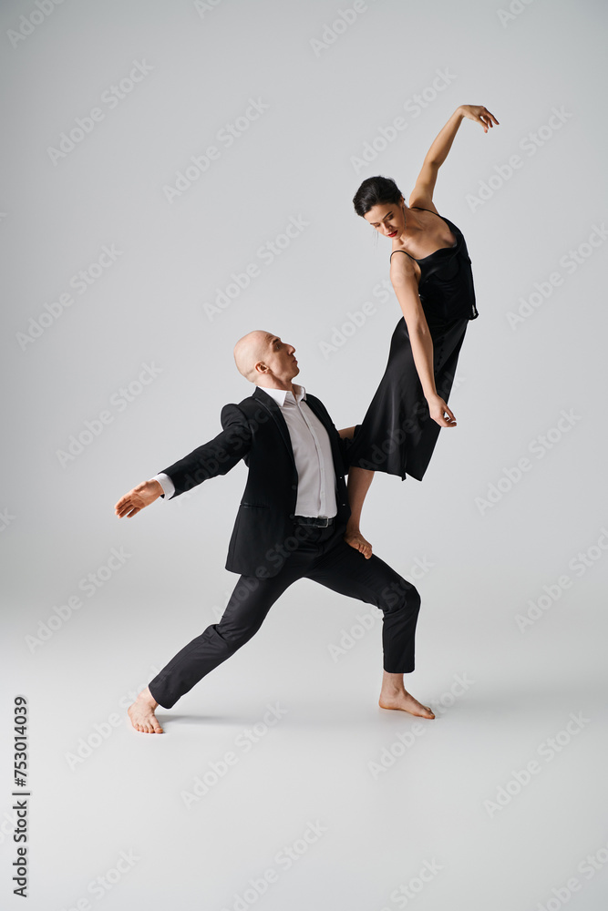 barefoot woman in black dress balancing gracefully on lap of dance partner in grey studio