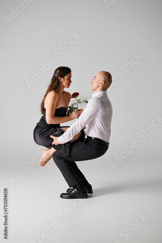 male dancer lying on the floor and lifting body of woman with red rose during dance performance