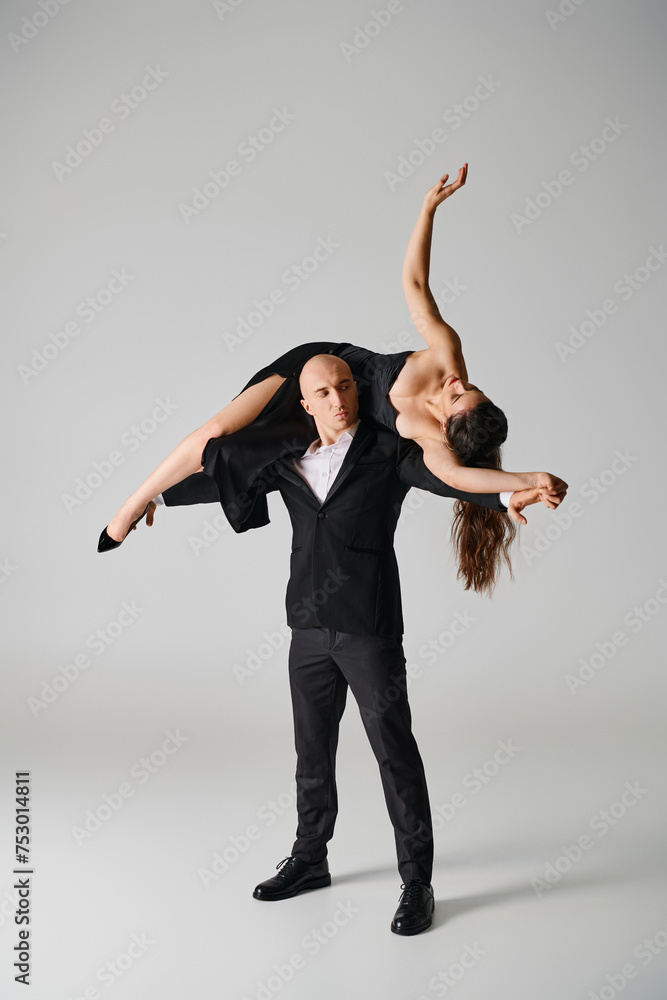 strong male dancer lifting brunette woman in dress and high heels in studio on grey background strong male dancer lifting brunette woman in dress and high heels in studio on grey background