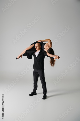 strong male dancer lifting brunette woman in dress and high heels on grey backdrop in studio