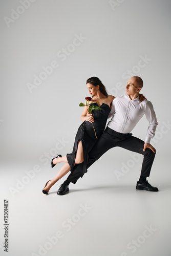 Elegant dance motion of young brunette couple, woman holding red rose and man performing in studio