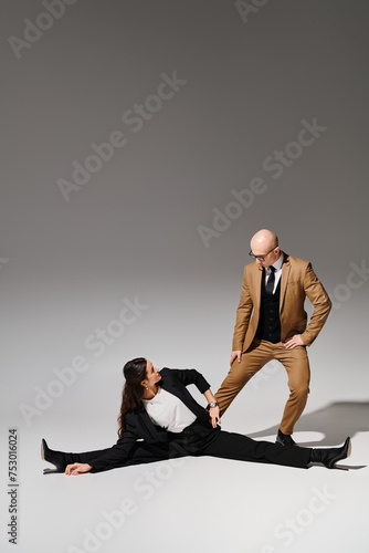 female acrobat in elegant corporate suits executing a split and holding hands with man in studio photo