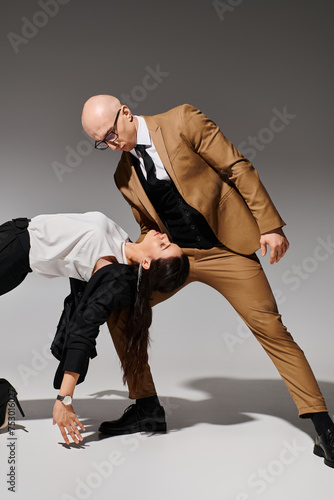 Business partners in a coordinated dance move, suited up together in the studio with grey backdrop photo