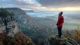 A woman clad in a red jacket gazes over a picturesque valley, embracing the tranquility of the morning.
