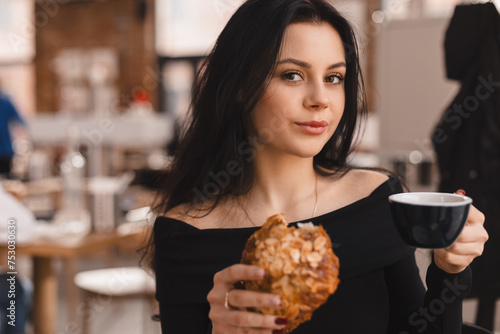 Photo of brunette teen woman ordering coffee and croissant. Young woman having breakfast with croissant and cup of coffee at the cafe.
