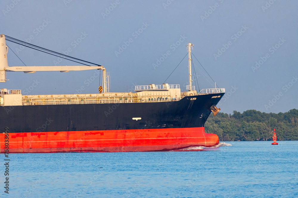 A cargo ship with a crane sails alongside the tropical coast