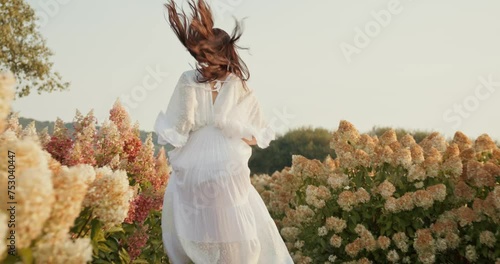 Beautiful girl running fast along the wide field with large colorful flowers.