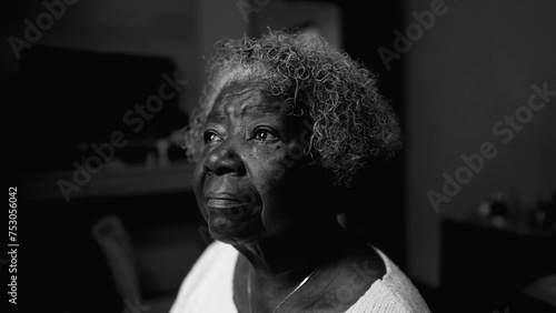 One introspective black senior woman in solitude at home in black and white. Monochromatic close-up face of an African American lady staring at window with thoughtful emotion