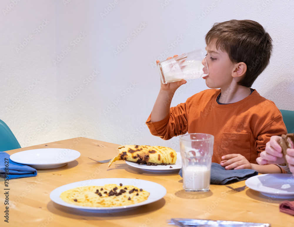 Boy having breakfast drinking a glass of milk and eating a pancake Boy having breakfast drinking a glass of milk and eating a pancake