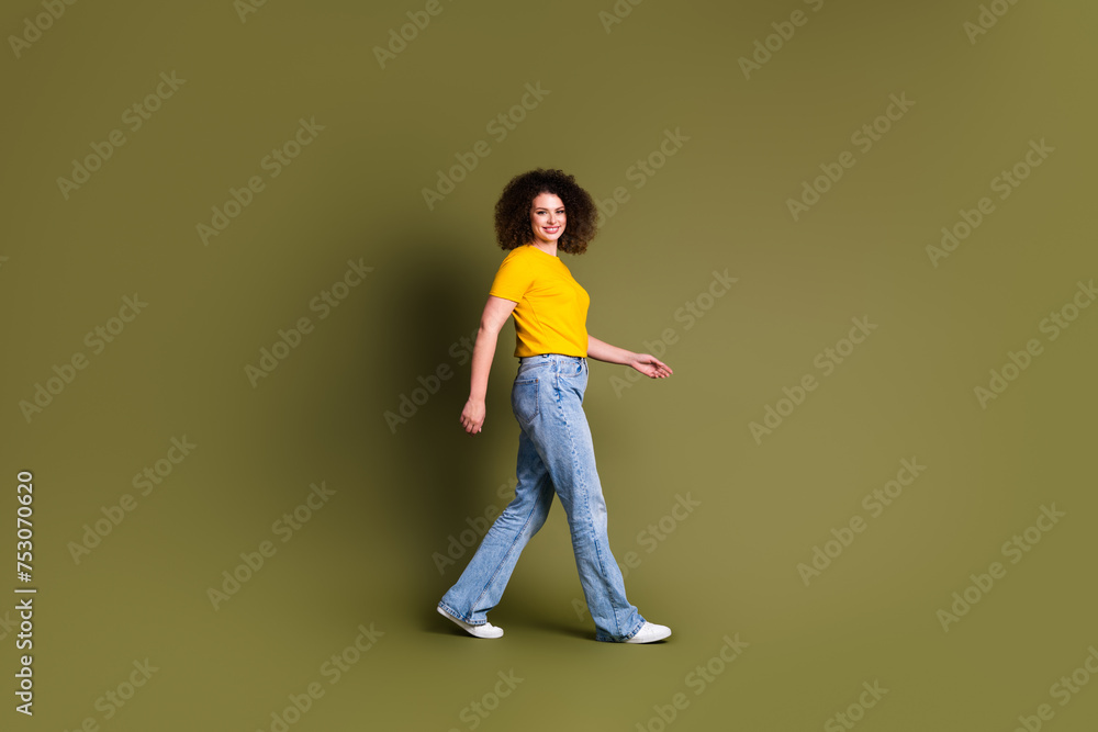 Full length body photo of cheerful young optimistic lady in yellow t shirt steps to next day satisfied isolated over khaki color background Full length body photo of cheerful young optimistic lady in yellow t shirt steps to next day satisfied isolated over khaki color background