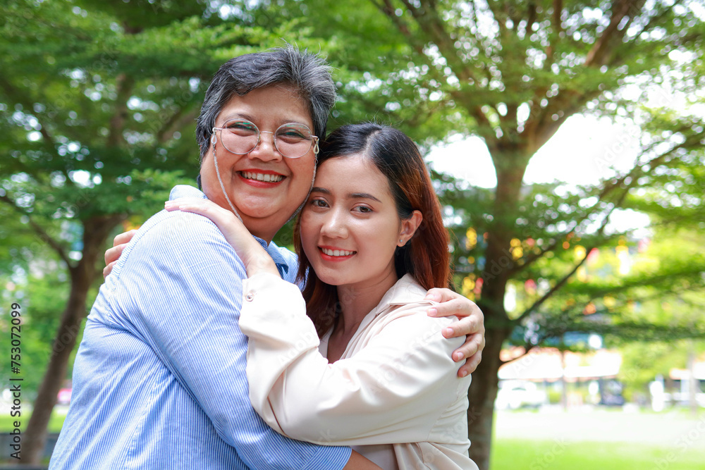 An elderly mother hugs her daughter, both smiling happily in the garden outside. Family concept. Health insurance An elderly mother hugs her daughter, both smiling happily in the garden outside. Family concept. Health insurance