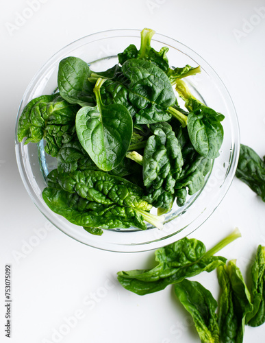 Fresh spinach leaves in a glass bowl with oil on white background.