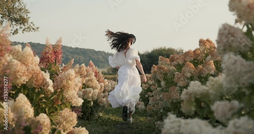 Beautiful girl running fast along the wide field with large colorful flowers.