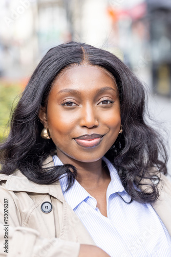 This striking close-up portrays a Black woman smiling warmly  her eyes twinkling with joy as she faces the camera. The urban setting blurs behind her  drawing attention to her radiant complexion and