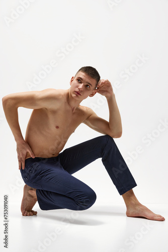 Handsome young man with short brunette hair, shirtless, muscular, relief body posing in jeans isolated over white studio background. Concept of sportive lifestyle, body and heath care, youth