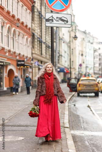 An elegant blonde in a red evening dress and fur coat is standing on the streets of the city, waiting for a taxi. Spring concept, international women's day. March 8 © Светлана Густова