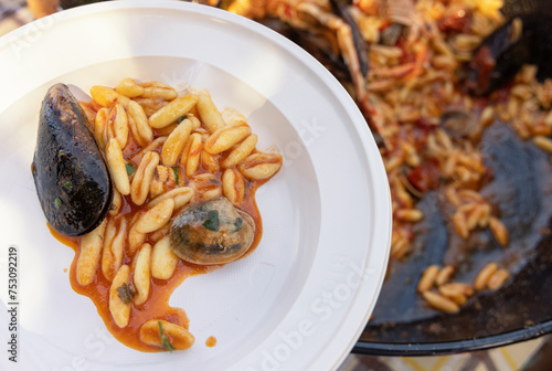 Plastic plate of pasta with black mussels, shrimps and tomatoes while it is served close up