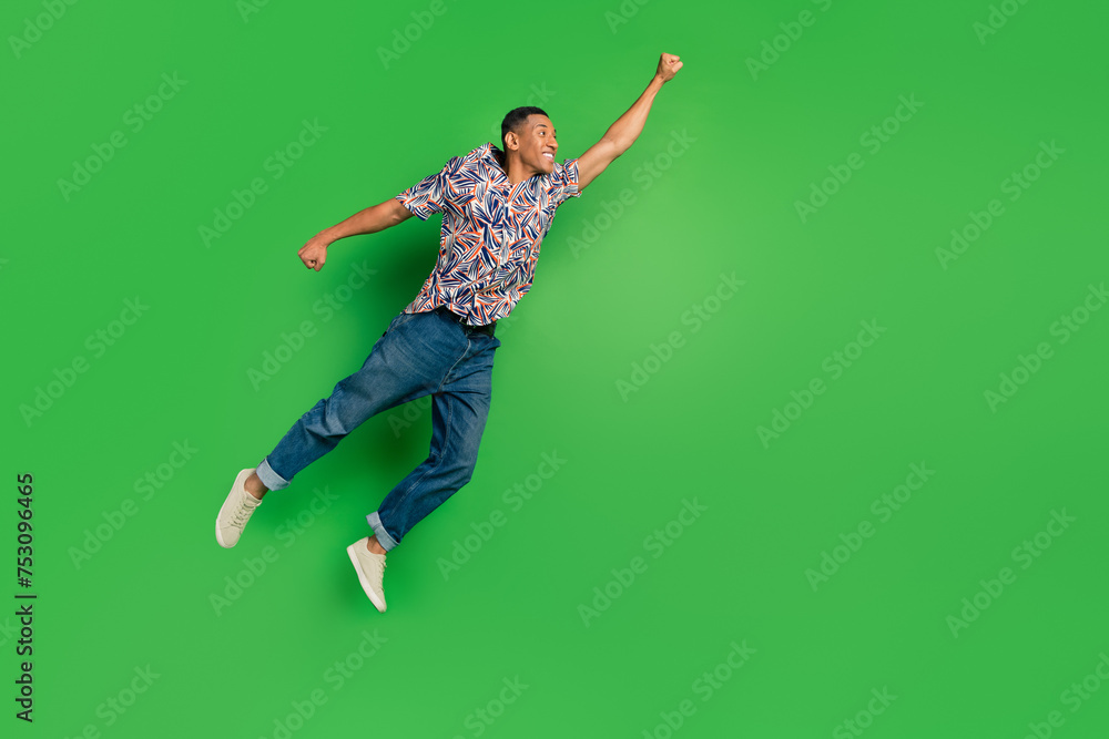 Full length photo of cheerful glad funky courageous man raise hand fly air empty space isolated on green color background Full length photo of cheerful glad funky courageous man raise hand fly air empty space isolated on green color background