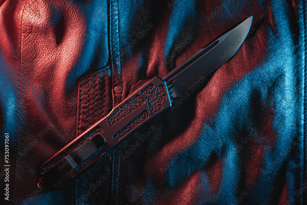 Close-up photo of a automatic folding knife on a leather jacket. - obrazy, fototapety, plakaty 