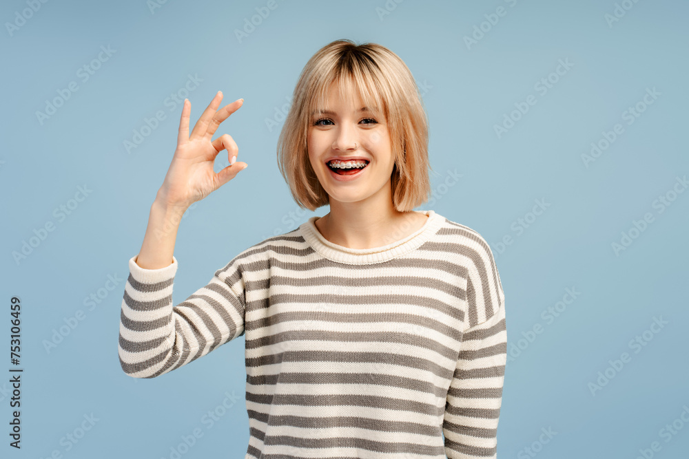 Happy blonde haired lady wearing braces gesturing okay while looking at the camera Happy blonde haired lady wearing braces gesturing okay while looking at the camera