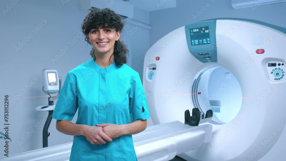Young tomography specialist posing with wide smile. Cheerful doctor smiling at background of MRI equipment. Cabinet for MRI examination. MRI specialist. Tomography technician. Medical specialist. Young tomography specialist posing with wide smile. Cheerful doctor smiling at background of MRI equipment. Cabinet for MRI examination. MRI specialist. Tomography technician. Medical specialist.