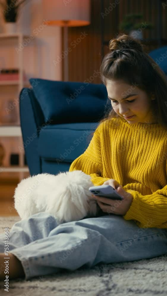 Teenage girl trying to text on cellphone and giving treats for active fluffy dog Teenage girl trying to text on cellphone and giving treats for active fluffy dog