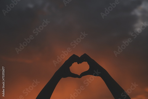 Silhouette of hands in heart symbol around the sun